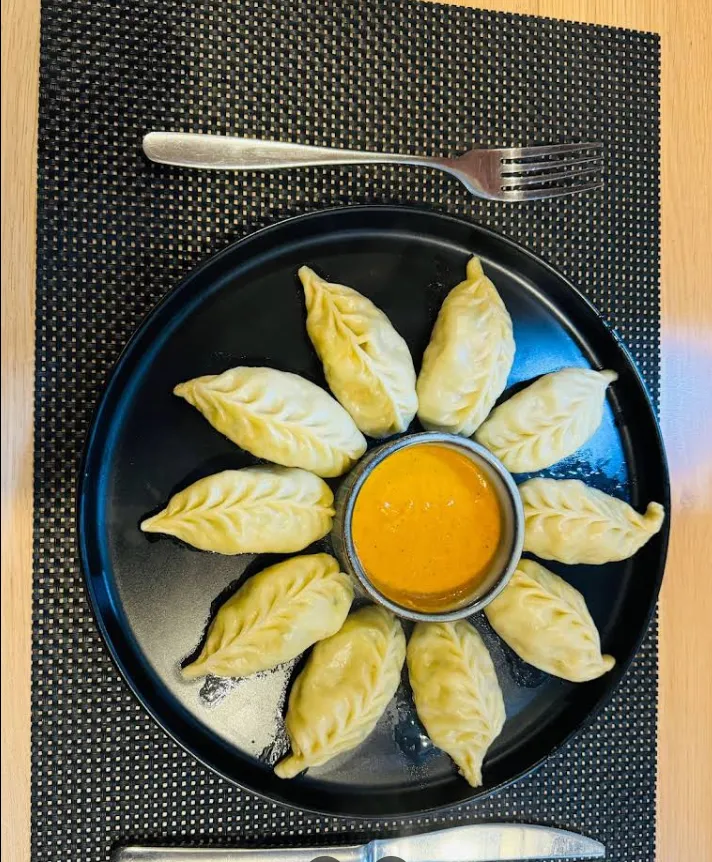A ring of steamed chicken momo around a bowl of orange achar