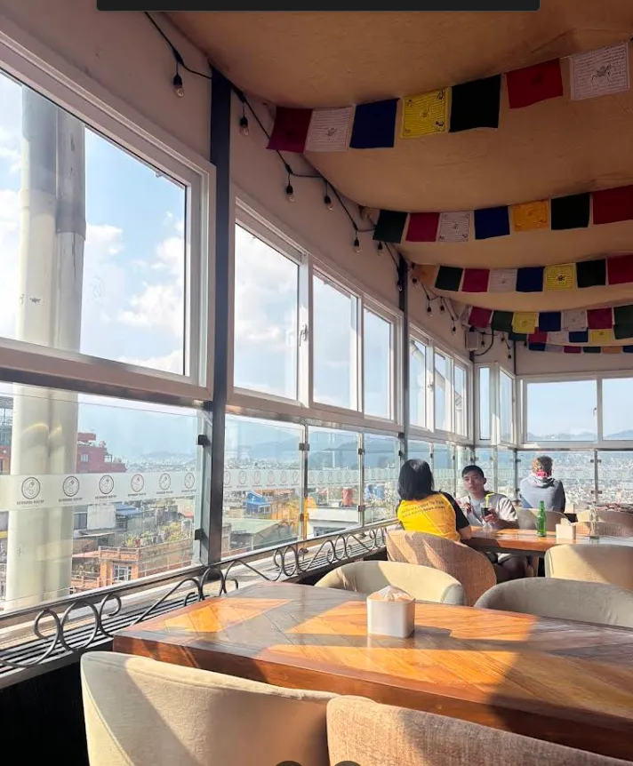 Open-air rooftop lounge with cushioned chairs, prayer flags and floor-to-ceiling views over the city