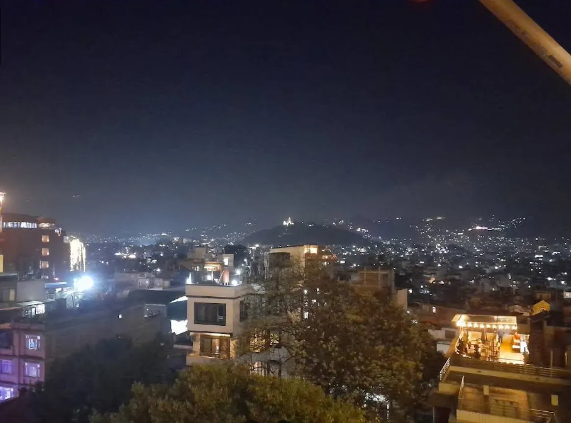 The Kathmandu skyline at night seen from the rooftop, city lights and the lit stupa in the distance